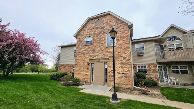 back of property featuring a lawn, a balcony, and brick siding