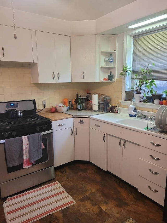 kitchen featuring white cabinets, a sink, stainless steel gas range oven, light countertops, and backsplash