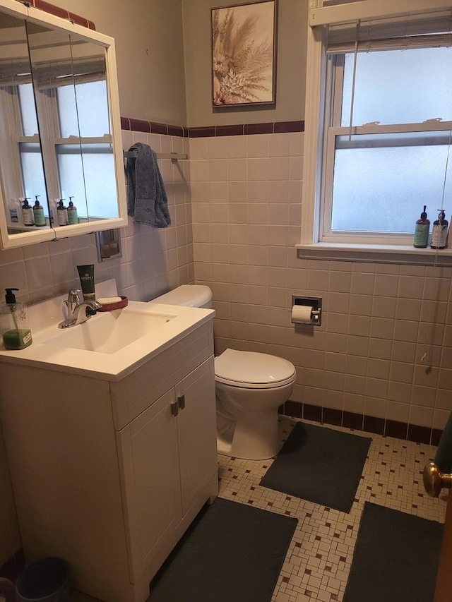 half bathroom with wainscoting, tile walls, vanity, and toilet