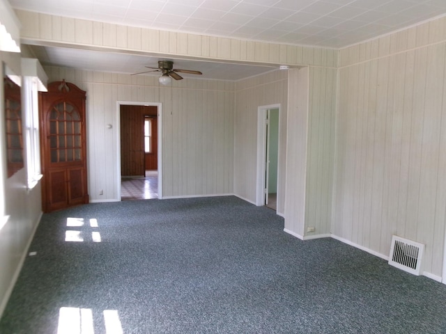spare room featuring visible vents, carpet flooring, a ceiling fan, and wooden walls