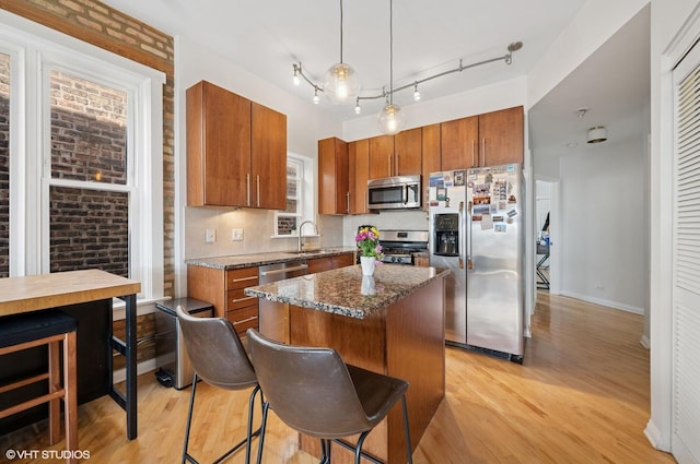 kitchen featuring a kitchen island, appliances with stainless steel finishes, brown cabinets, light wood-type flooring, and dark stone countertops