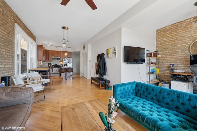 living room featuring brick wall, ceiling fan, rail lighting, and light wood-style floors