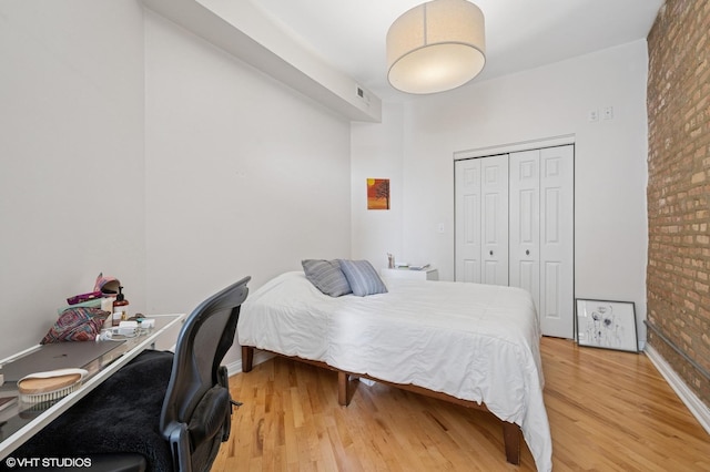 bedroom with brick wall, visible vents, baseboards, a closet, and light wood-style flooring