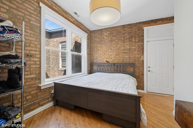 bedroom featuring wood finished floors, baseboards, brick wall, and visible vents