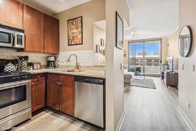 kitchen featuring light wood-style floors, light stone counters, a sink, backsplash, and stainless steel appliances