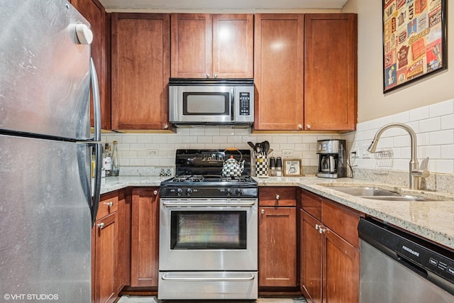 kitchen with brown cabinets, light stone countertops, appliances with stainless steel finishes, a sink, and tasteful backsplash