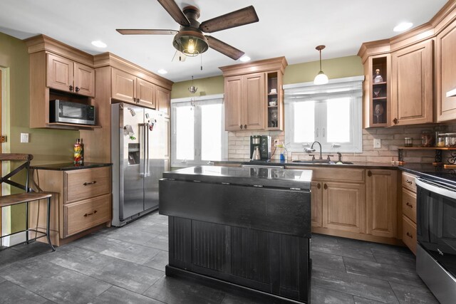 kitchen with dark countertops, appliances with stainless steel finishes, a sink, a ceiling fan, and decorative backsplash