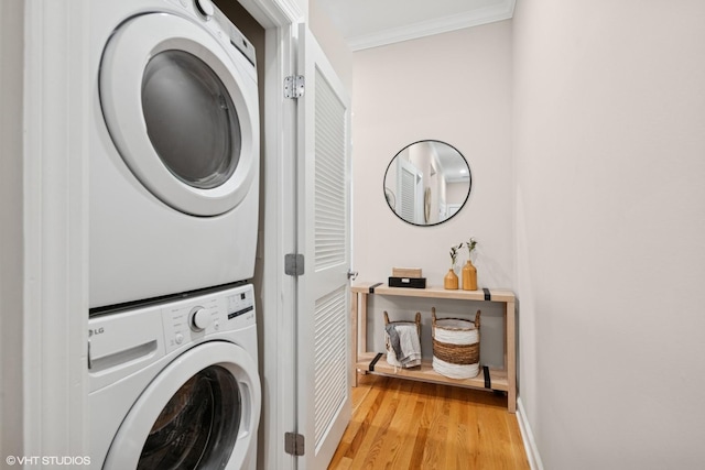 laundry room featuring laundry area, crown molding, baseboards, light wood finished floors, and stacked washer / drying machine