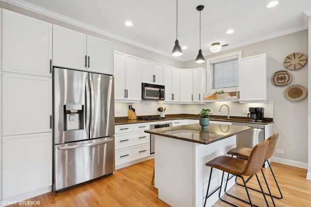 kitchen with a kitchen island, a kitchen bar, white cabinets, a sink, and appliances with stainless steel finishes