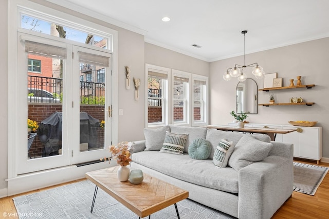 living room with baseboards, ornamental molding, light wood-style flooring, and a notable chandelier