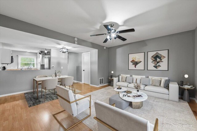living room with visible vents, light wood-style flooring, ceiling fan, and baseboards