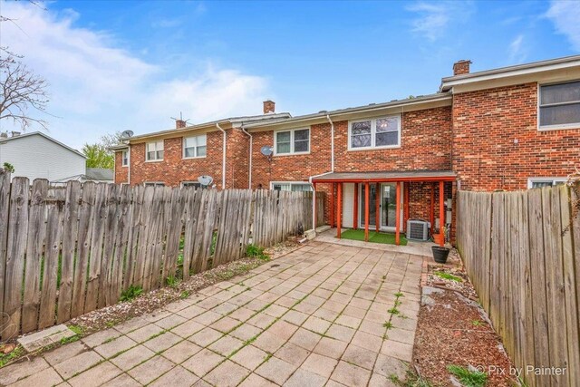 rear view of house featuring brick siding, central air condition unit, a chimney, and a patio