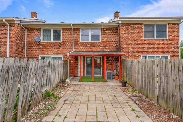 rear view of house featuring brick siding, central AC unit, a chimney, and a patio