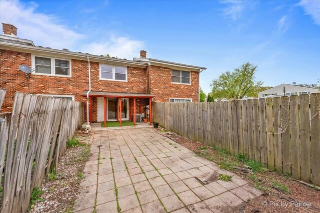 rear view of house with brick siding, a chimney, a fenced backyard, and a patio area