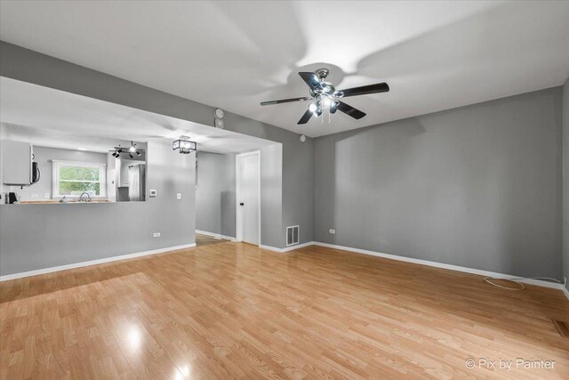 empty room featuring light wood-style floors, baseboards, ceiling fan with notable chandelier, and visible vents