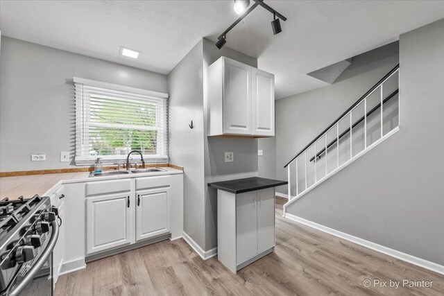 kitchen with rail lighting, light wood-type flooring, stainless steel gas stove, a sink, and white cabinets