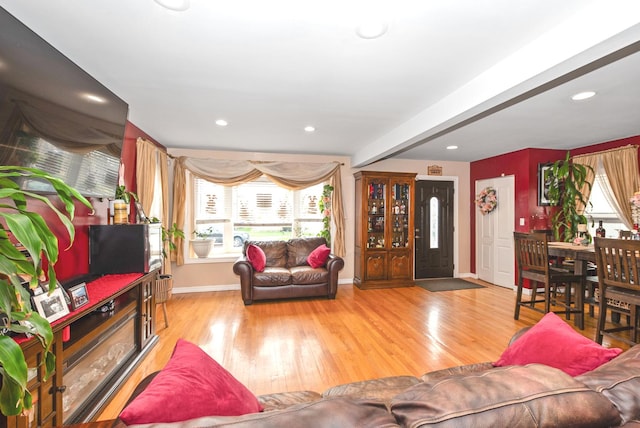 living area with baseboards, a healthy amount of sunlight, beam ceiling, and wood finished floors