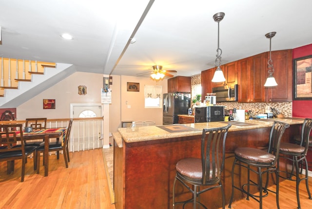 kitchen with a ceiling fan, light wood-style flooring, a breakfast bar, and stainless steel appliances