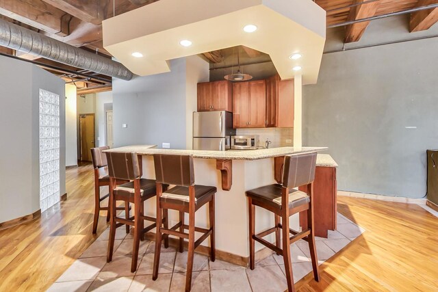 kitchen with a breakfast bar, baseboards, brown cabinets, light wood-style flooring, and stainless steel appliances