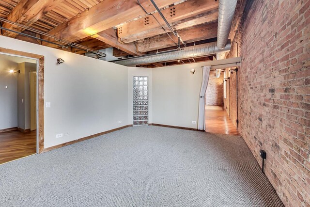 carpeted empty room with baseboards and brick wall