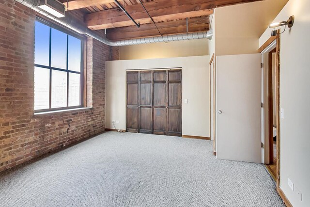 unfurnished bedroom with carpet, beam ceiling, brick wall, and wooden ceiling