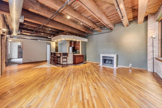 unfurnished living room featuring baseboards, wooden ceiling, light wood-type flooring, a tile fireplace, and beamed ceiling