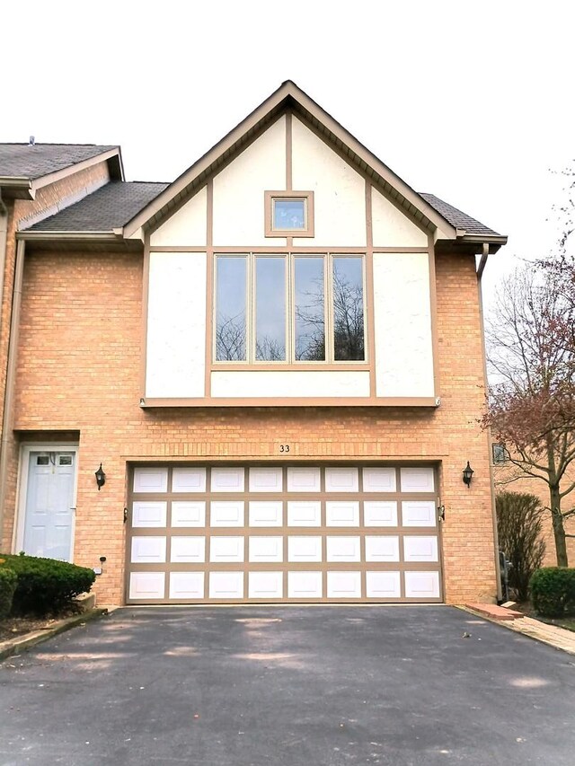 view of front of house featuring an attached garage, a shingled roof, aphalt driveway, and brick siding