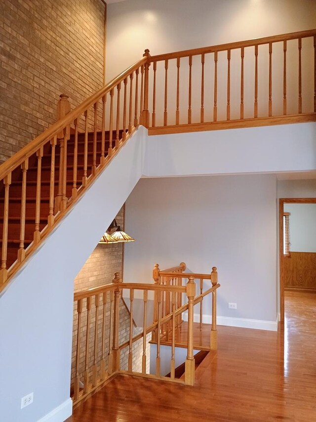 stairway with baseboards, brick wall, wood finished floors, and a towering ceiling