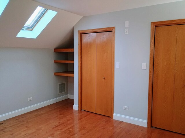 unfurnished bedroom with visible vents, light wood finished floors, baseboards, and vaulted ceiling with skylight