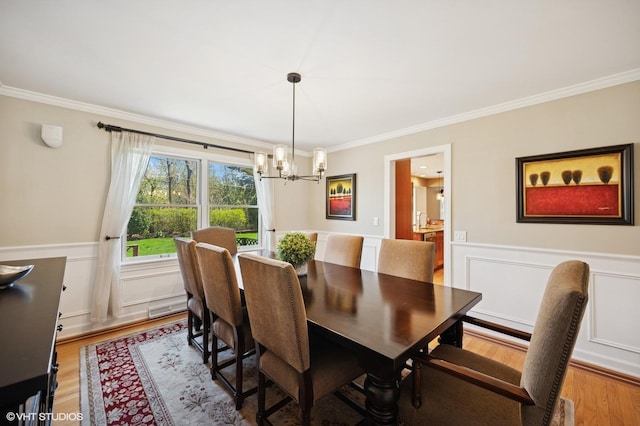 dining room featuring light wood-type flooring, ornamental molding, wainscoting, and a chandelier