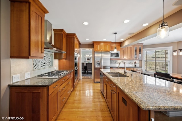 kitchen featuring wall chimney range hood, brown cabinets, appliances with stainless steel finishes, and a sink
