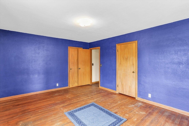 unfurnished bedroom featuring baseboards, a textured wall, and wood finished floors