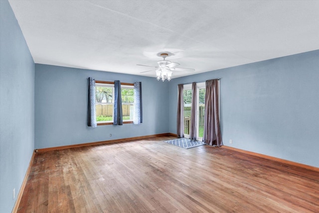 spare room with baseboards, a ceiling fan, wood finished floors, and a wealth of natural light