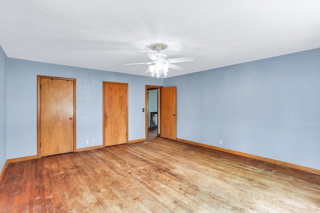unfurnished bedroom with baseboards, a ceiling fan, multiple closets, and wood finished floors