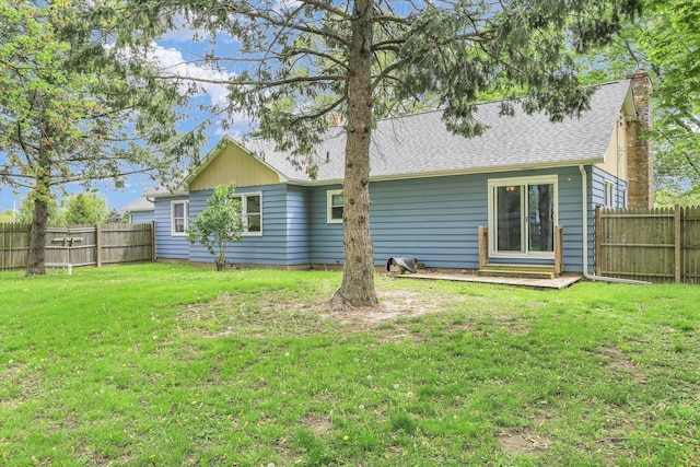 back of house with a lawn, a shingled roof, a chimney, and a fenced backyard