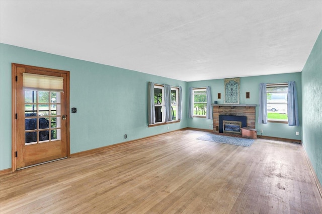 unfurnished living room with a stone fireplace, baseboards, and wood finished floors