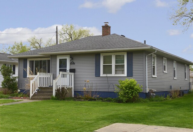 rear view of house with a lawn, a chimney, and roof with shingles