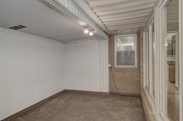 spare room featuring carpet floors, brick wall, and visible vents