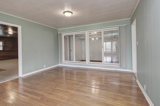 unfurnished room featuring wood-type flooring, ornamental molding, baseboards, and wood walls