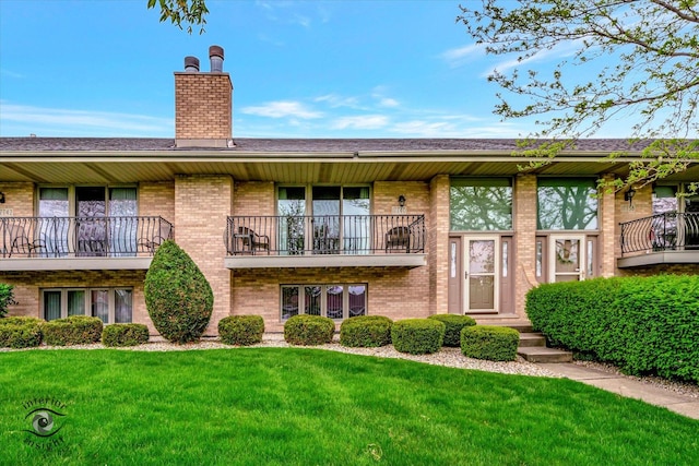 view of front of home featuring a balcony, brick siding, a front yard, and a chimney