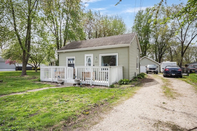 view of front of house with a garage, a front lawn, a wooden deck, roof with shingles, and driveway