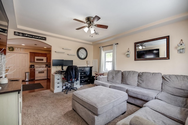 living room with a ceiling fan, a raised ceiling, and light carpet