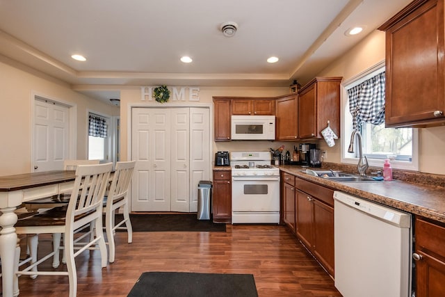 kitchen featuring brown cabinets, a sink, a raised ceiling, white appliances, and dark wood-type flooring