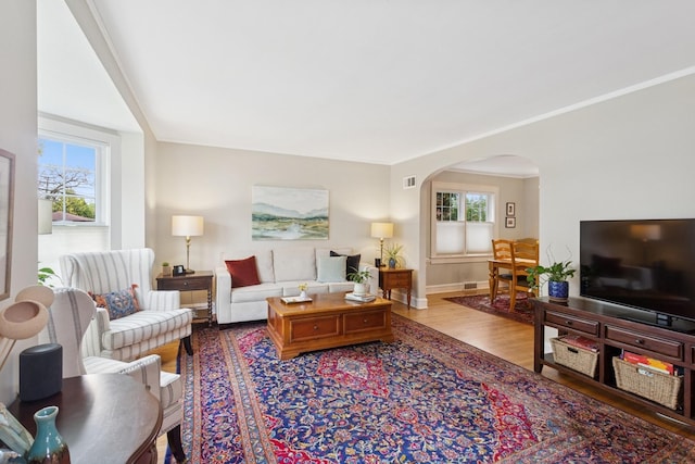 living room featuring arched walkways, baseboards, visible vents, and wood finished floors