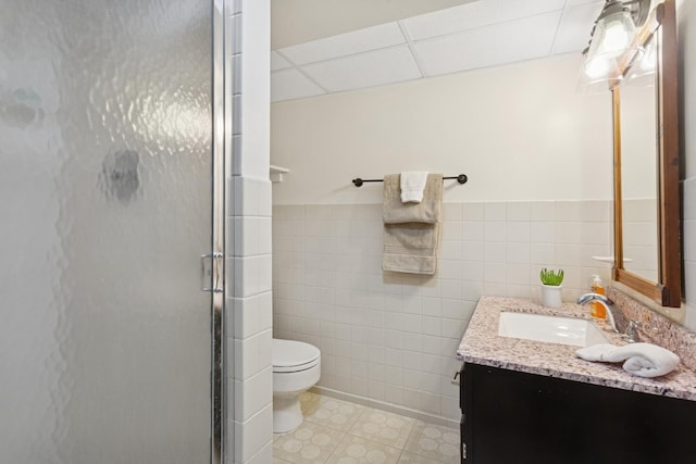 bathroom with tile walls, toilet, a shower stall, and a paneled ceiling