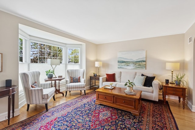 living room with baseboards, crown molding, visible vents, and light wood-type flooring
