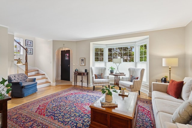 living room with arched walkways, stairs, ornamental molding, and wood finished floors