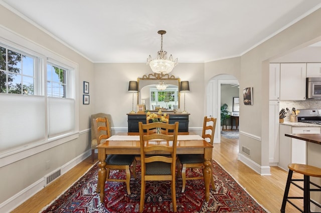 dining room with ornamental molding, light wood finished floors, an inviting chandelier, visible vents, and arched walkways