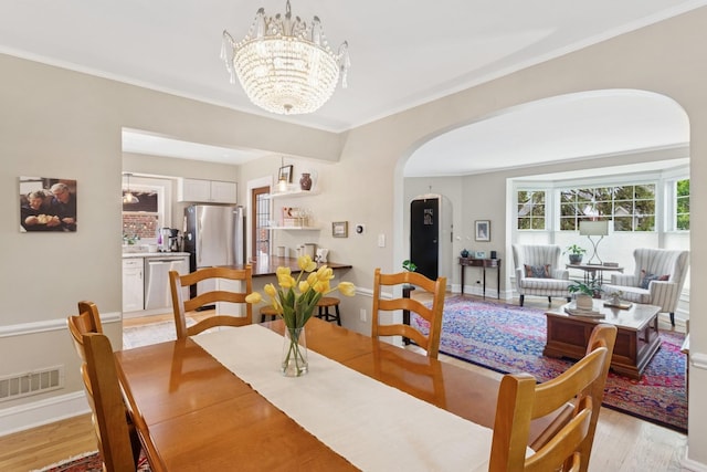dining space with an inviting chandelier, light wood-style flooring, visible vents, arched walkways, and ornamental molding
