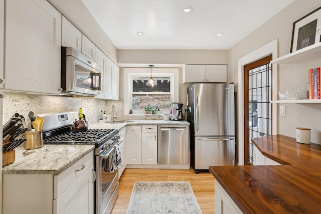 kitchen with wooden counters, backsplash, light wood-style floors, stainless steel appliances, and white cabinets